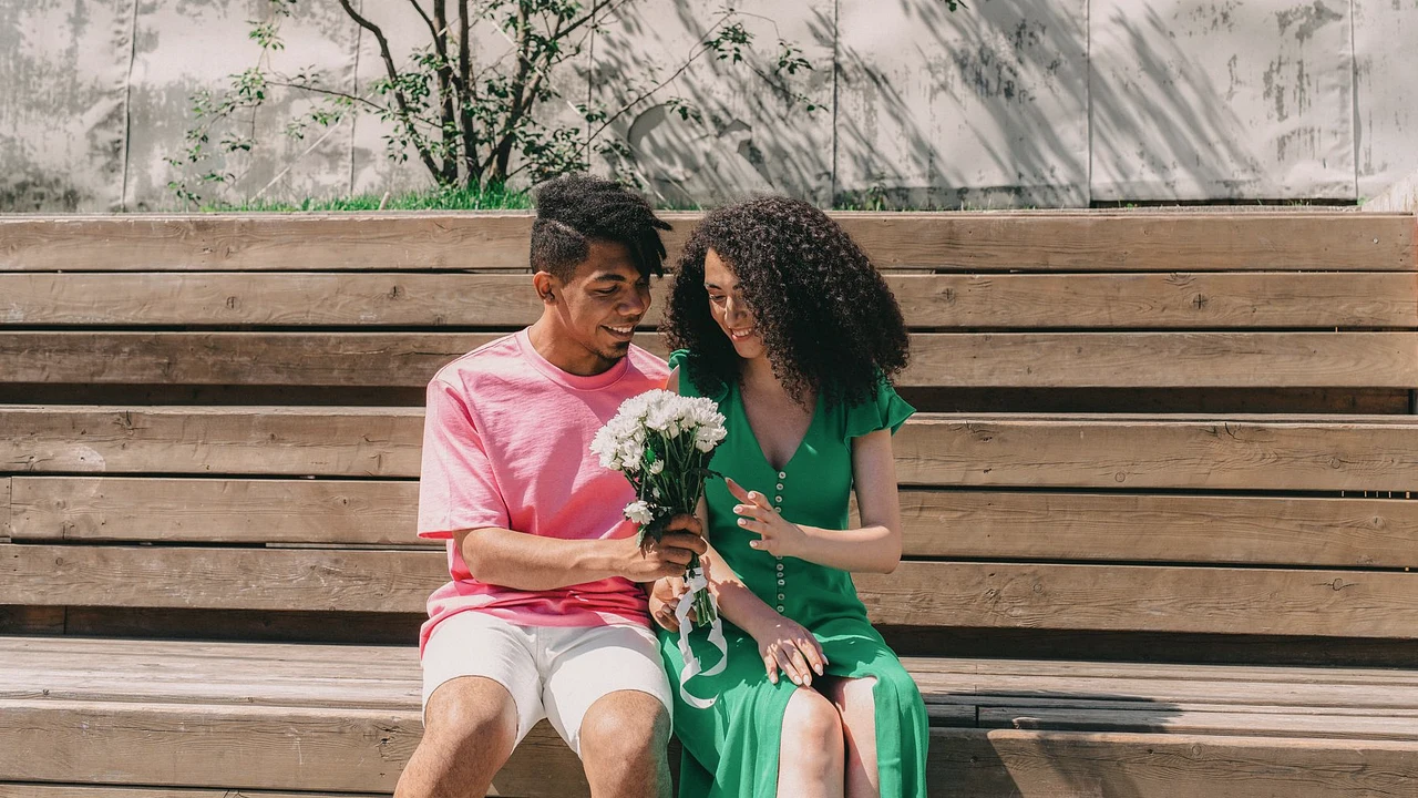 A man giving a bouquet of flowers to a woman while they sit together outdoors