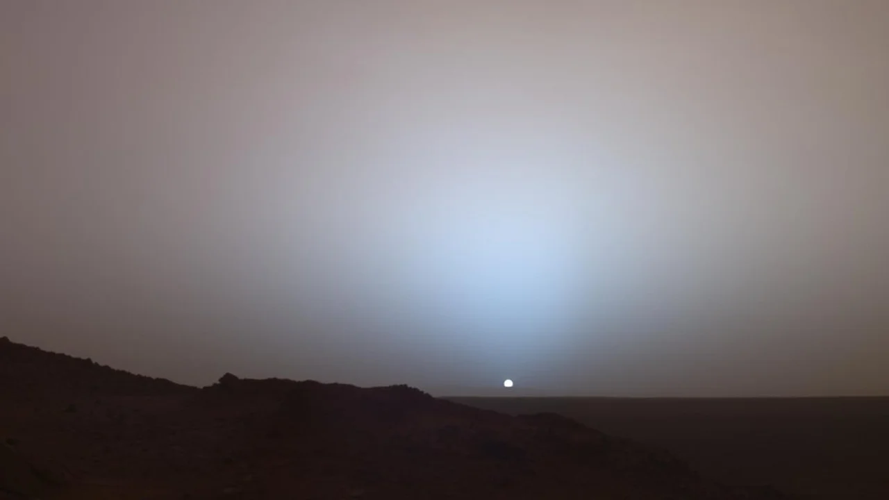 The Sun setting beneath a blue glow above the rim of Gusev crater on Mars