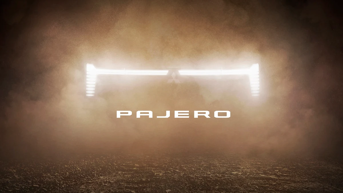 Official Mitsubishi teaser showing the Pajero name and a bright front lighting signature emerging through dust