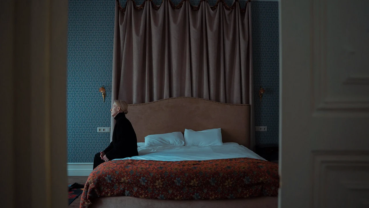 A woman sitting alone on a bed in a quiet room after an emotionally difficult moment