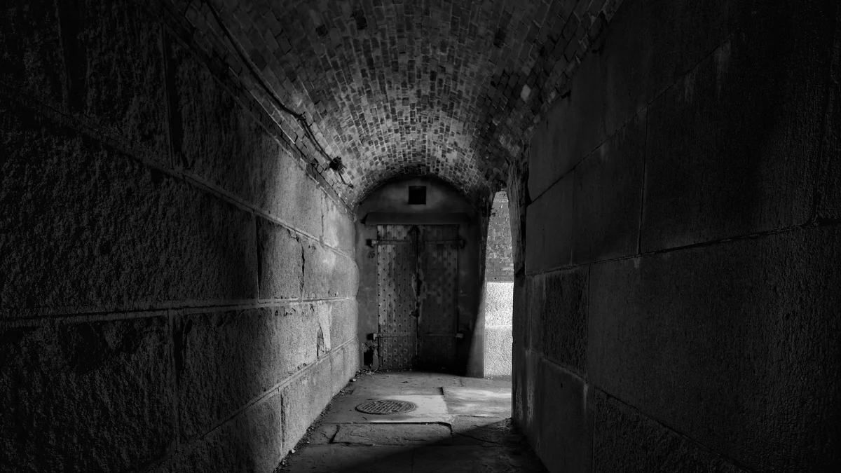 A dark stone tunnel opening into a sharply brighter sunlit doorway