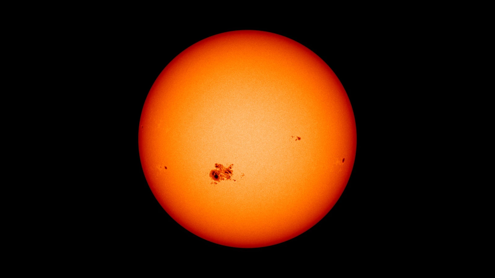 A NASA Solar Dynamics Observatory HMI intensity image shows a large, already-visible sunspot group on the orange solar disk against black space