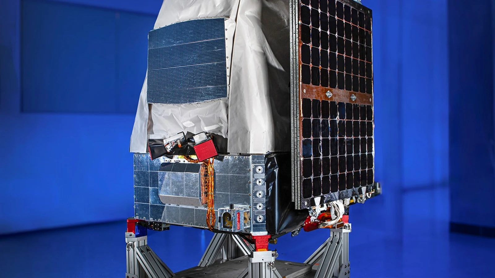 NASA photograph of the fully integrated Pandora spacecraft on a support frame, with its telescope, insulation and solar panel visible against a blue-lit test room
