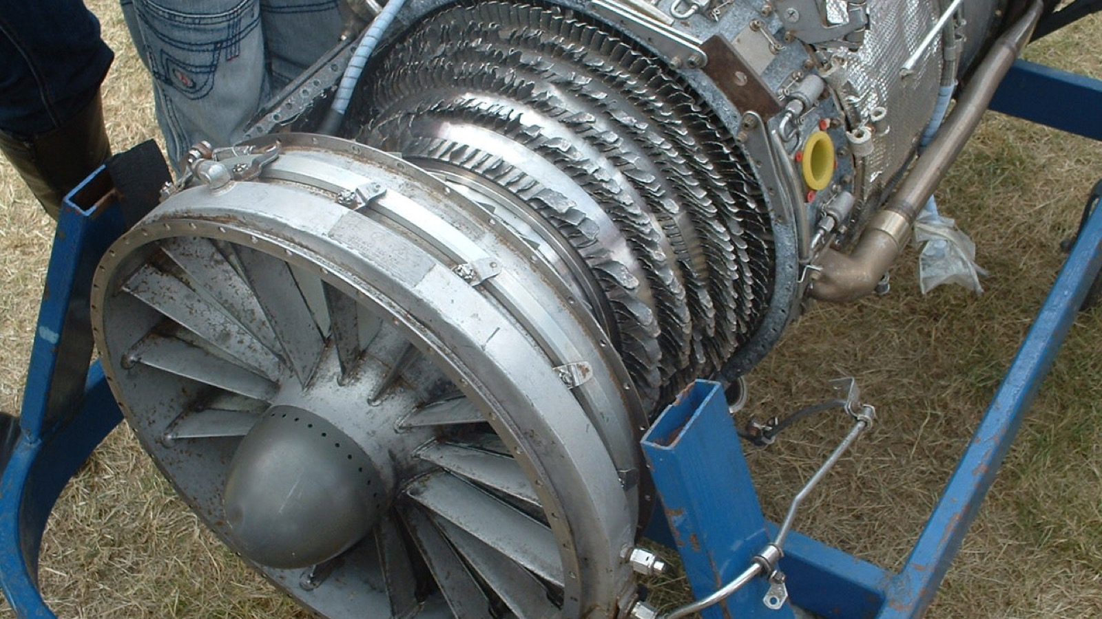 A damaged jet engine on a blue maintenance stand, showing the exposed front fan and distorted rows of blades after a bird strike