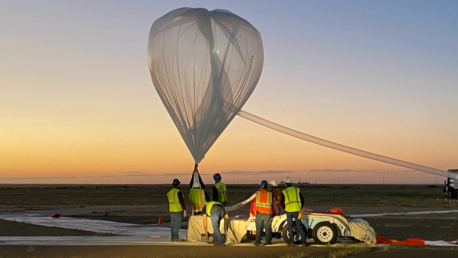 NASA photograph of a scientific balloon inflating at sunrise with its flight train and support crew on the ground