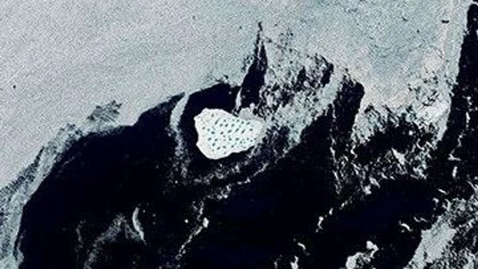 NASA Landsat view of a white Greenland iceberg with blue meltwater ponds surrounded by dark water and sea ice