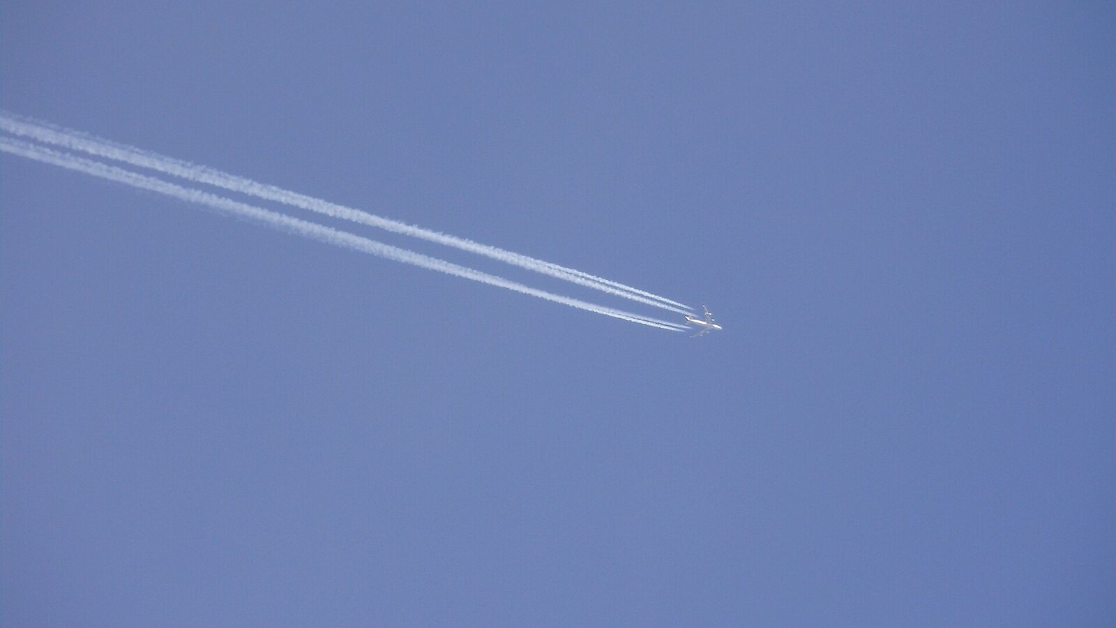 A Boeing 747 high in a blue sky producing four narrow white condensation trails